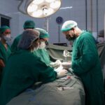 Foto da equipe do Hospital Municipal de Araguaína em uma das cirurgias urológicas pediátricas. Há três profissionais em destaque. Eles olham para baixo, onde está o paciente. Um dos médicos segura uma pinça.