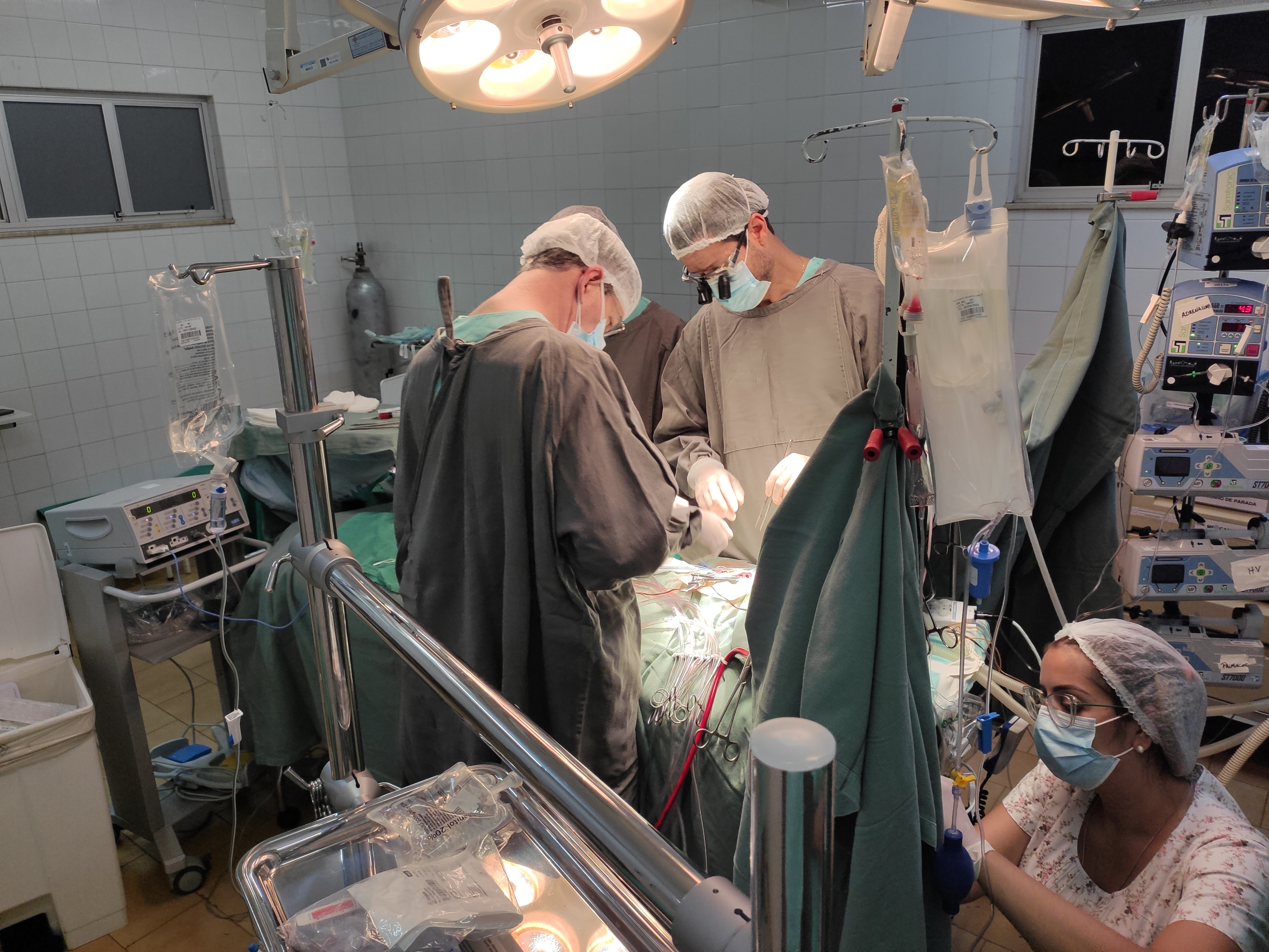 Imagem do centro cirúrgico e da equipe médica realizando procedimento na mesa de cirurgia.