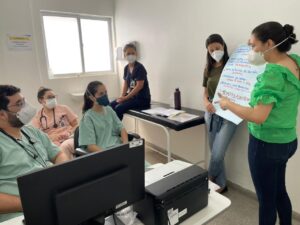 Duas pessoas estão de pé segurando um cartaz. Outras pessoas estão sentadas.